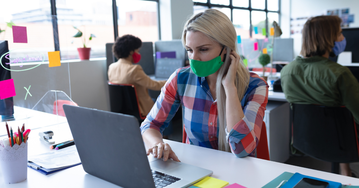 Woman in mask at desk in office workplace