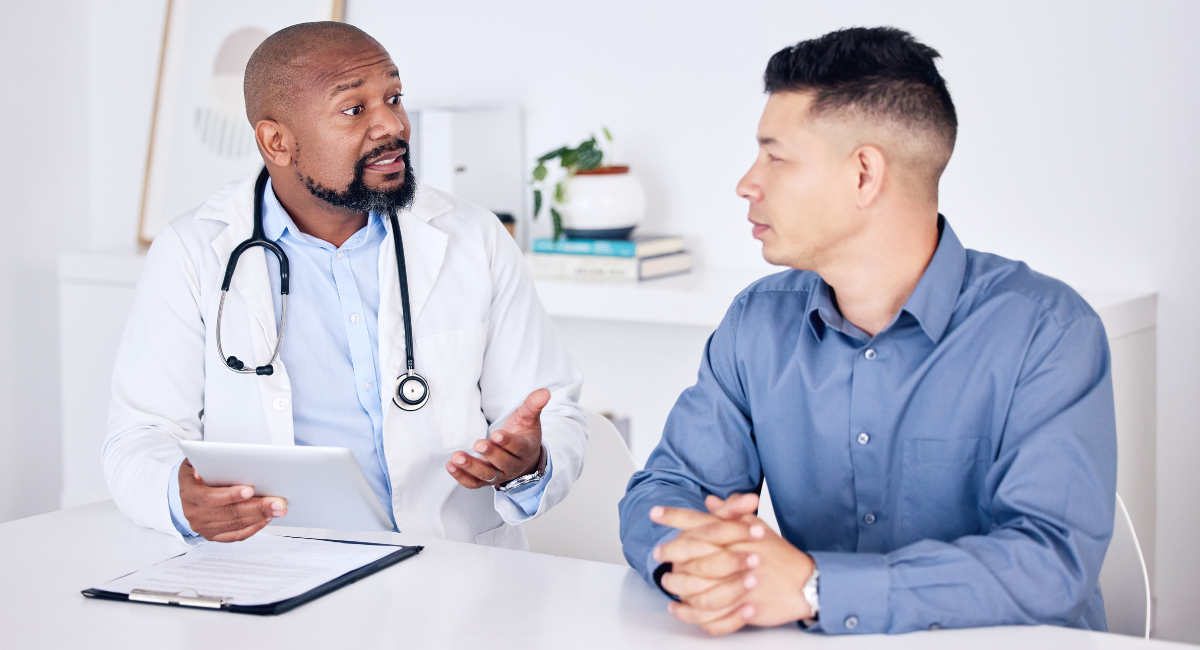 A male doctor is seated at a table with a male patient who is in his 40s. They are discussing the importance of erectile dysfunction, or impotence.