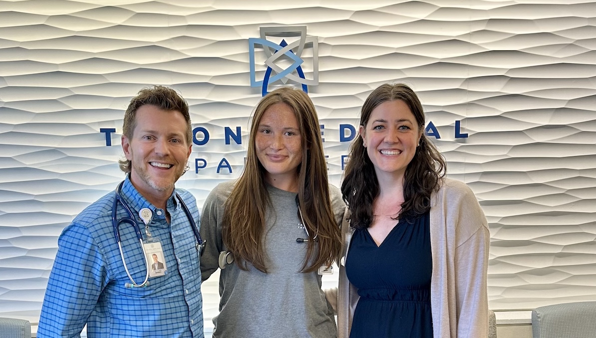 2025 internal medicine medical assistant intern Lily Suyao is pictured in front of a textured wall at Tryon Medical Partners, with her mentors, Dr. Ryan Shelton to her right, and PA-C Tristan Lunde to her left.