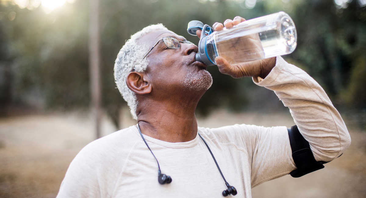 An older African American man in glasses drinks water from a sports bottle after exercising outside