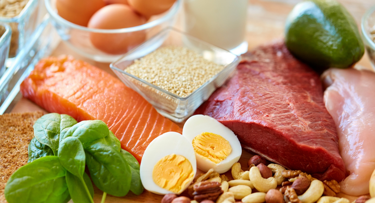 An attractive array of healthy foods that are high in protein, including chicken, lean beef, hard boiled eggs, mixed nuts, salmon, and spinach