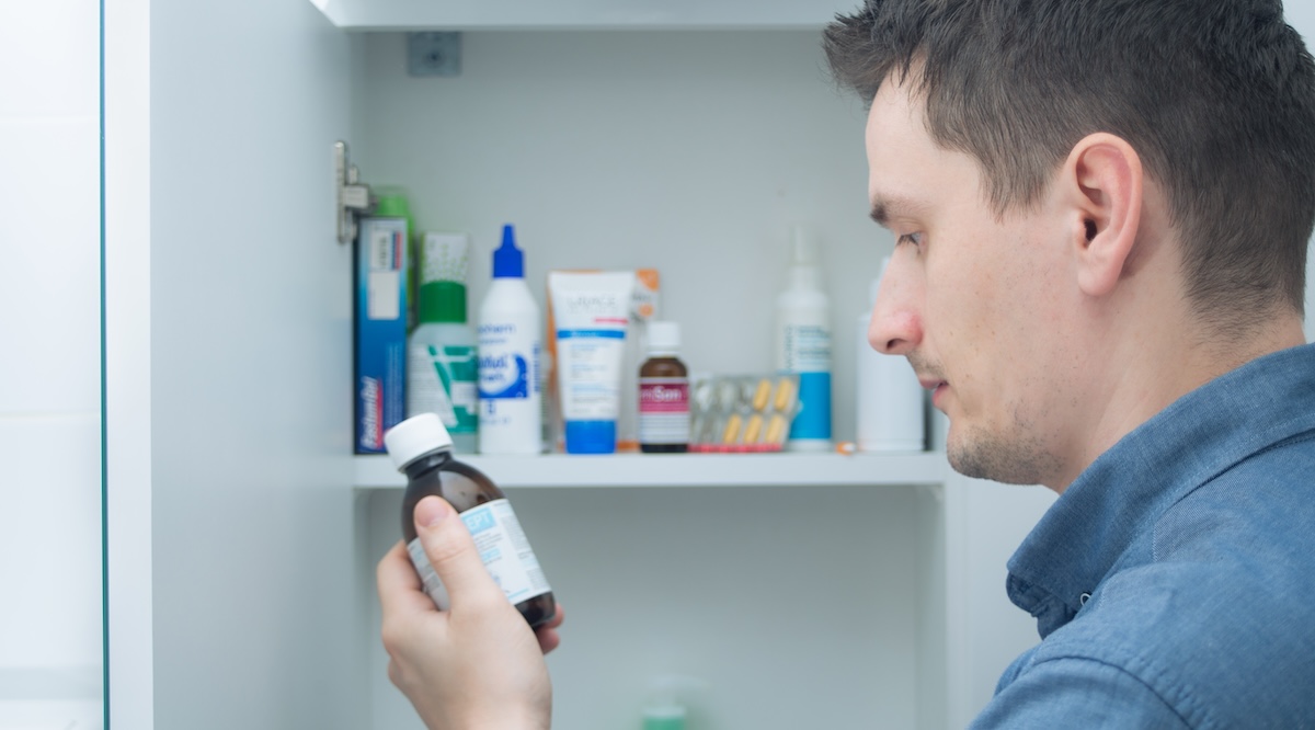 Man holds medication bottle reading instruction or prescription on packaging. Man looking at bottles from medicine cabinet